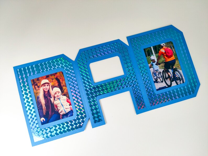 May include: Blue cardstock frame with a holographic finish, shaped like the word "DAD". The frame has three openings for photos, two of which are filled with photos of people.