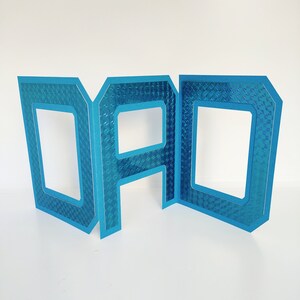 May include: Blue cardboard letters spelling "DAD" with a textured, iridescent finish. Each letter has a cutout in the center.