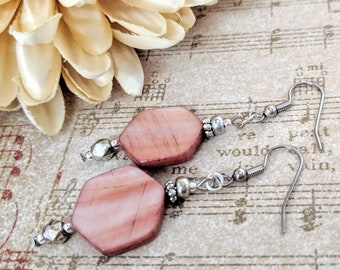 May include: A pair of earrings with pink and white hexagonal shell beads and silver metal accents. The earrings have a simple design and are perfect for everyday wear.