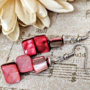 May include: A pair of red and pink shell earrings with silver hooks. The earrings are made of stacked square-shaped shells.