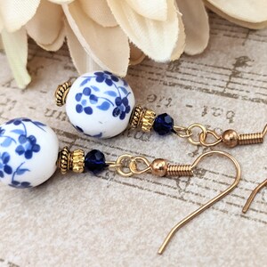 May include: A pair of blue and white porcelain earrings with gold accents and blue crystal beads. The earrings are on a gold background.