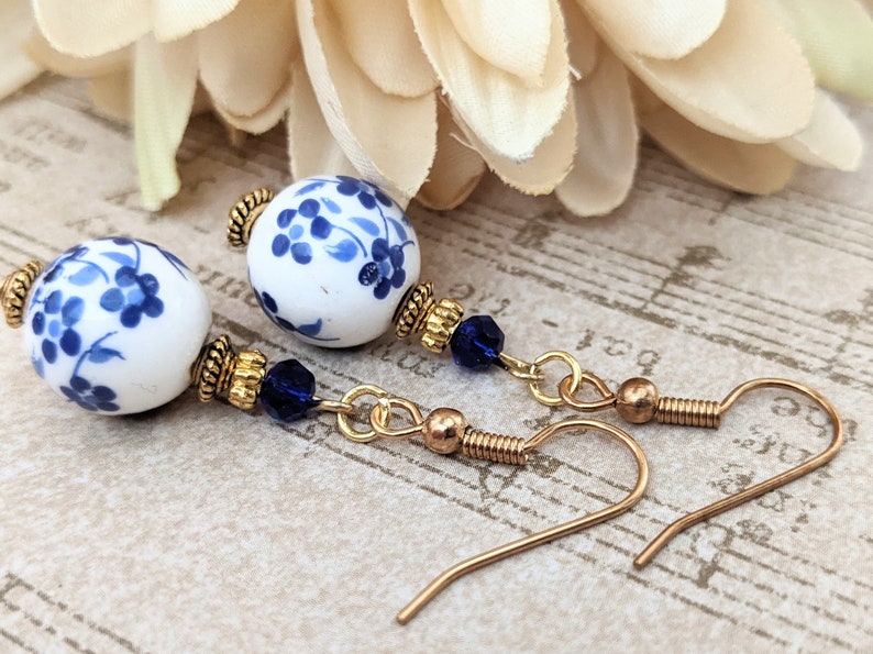 May include: A pair of blue and white porcelain bead earrings with gold accents and blue crystal beads hanging from gold chains.