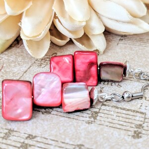 May include: Pink and red square shaped earrings with silver hooks. The earrings are made of shell and have a pearlescent finish.