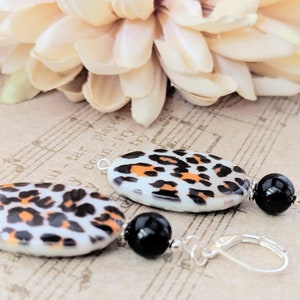 May include: A pair of dangle earrings with oval-shaped black and white leopard print ceramic beads and black onyx beads. The earrings have silver leverback closures.