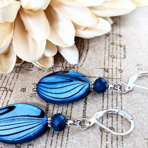 May include: A pair of blue and black oval earrings with silver leverback closures. Each earring features a blue oval bead with black swirling lines and a smaller dark blue crystal bead.