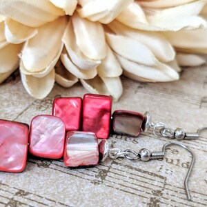 May include: Pink and red square shaped earrings with silver hooks. The earrings are made of shell and have a pearlescent finish.