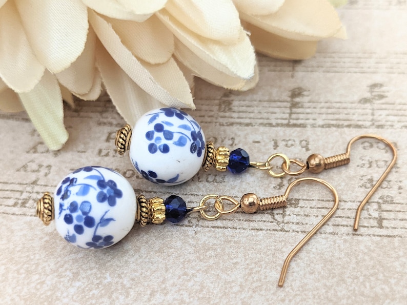 May include: A pair of gold dangle earrings with blue and white porcelain beads and blue crystal accents.