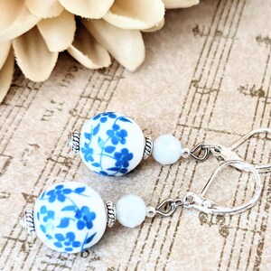 May include: White and blue porcelain bead earrings with a silver hook closure. The beads feature a floral design with blue flowers and leaves on a white background.