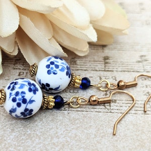 May include: A pair of blue and white porcelain dangle earrings with gold accents and blue crystal beads. The earrings have a floral design.