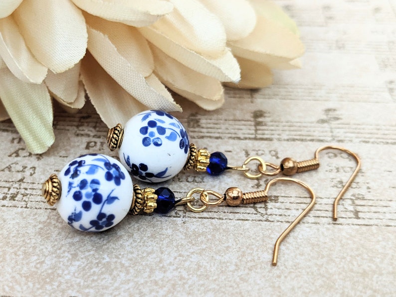 May include: A pair of blue and white porcelain dangle earrings with gold accents and blue crystal beads. The earrings have a floral design.