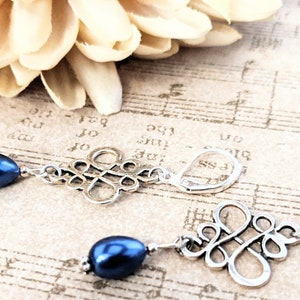 May include: A pair of silver earrings with a blue pearl drop and a silver knot design.