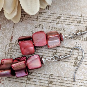 May include: A pair of red and silver earrings with a teardrop shape. The earrings are made of red shell beads and silver hooks.