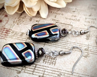 May include: A pair of black and iridescent glass earrings with geometric patterns. The earrings have silver hooks and a small brown bead on each earring.
