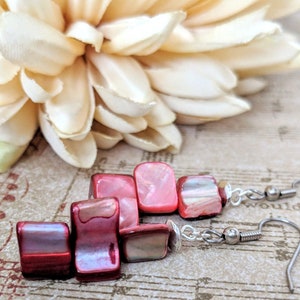 May include: A pair of dangle earrings with red and pink shell beads and silver hooks.