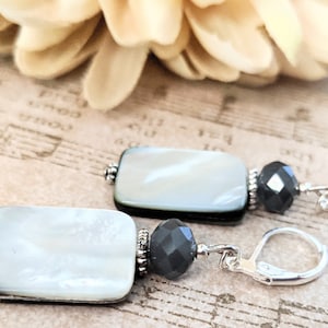 Può includere: Un paio di orecchini pendenti in argento con accenti di conchiglia bianca e perline sfaccettate nere.