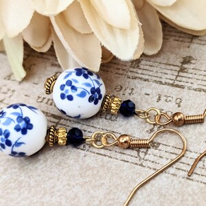 May include: A pair of dangle earrings with blue and white porcelain beads and gold accents. The beads feature a floral design.