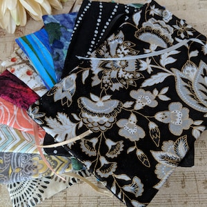 May include: A stack of fabric pouches with various patterns, including floral, geometric, and abstract designs. The pouches are made of different fabrics, including cotton and linen. The pouches are tied together with a ribbon.