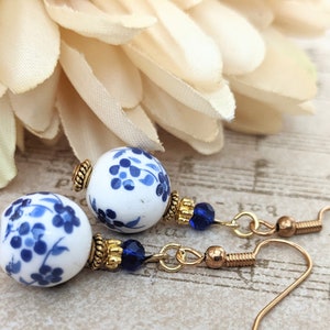 May include: A pair of blue and white porcelain dangle earrings with gold accents and blue crystal beads. The earrings feature a floral design.