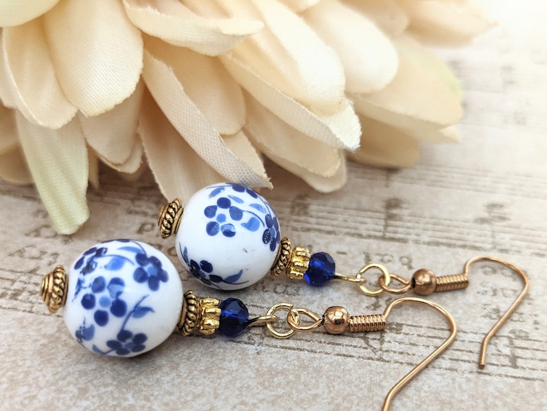 May include: A pair of blue and white porcelain dangle earrings with gold accents and blue crystal beads. The earrings feature a floral design.