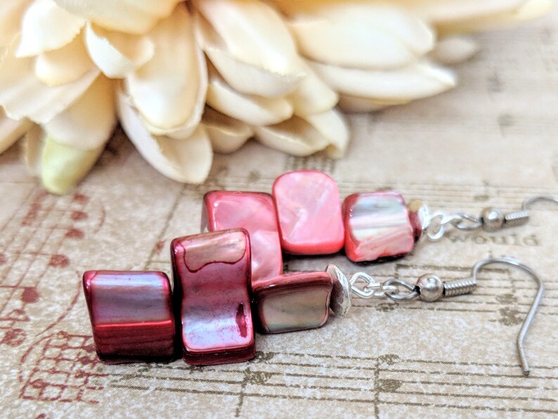 May include: A pair of dangle earrings with red and pink iridescent shell beads. The earrings have silver hooks.