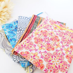 May include: Five fabric pouches with different colorful patterns. The pouches are made of cotton and have a drawstring closure. The pouches are stacked on top of each other.