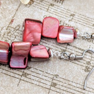 May include: Red and iridescent square-shaped earrings with silver hooks. The earrings are made of multiple pieces of red stone.