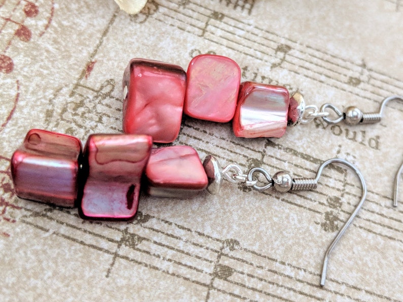 May include: Red and iridescent square-shaped earrings with silver hooks. The earrings are made of multiple pieces of red stone.