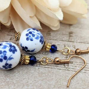 May include: A pair of blue and white porcelain earrings with gold accents and blue crystal beads. The earrings have a floral design and are suspended from gold hooks.
