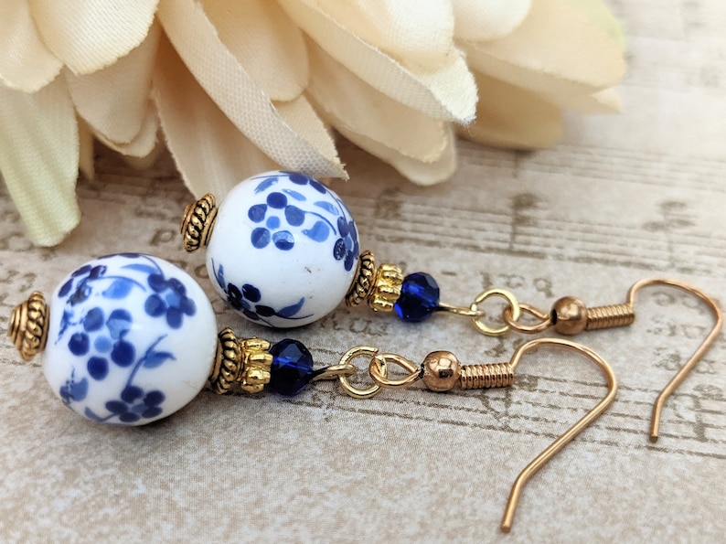 May include: A pair of blue and white porcelain earrings with gold accents and blue crystal beads. The earrings have a floral design and are suspended from gold hooks.