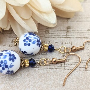 May include: A pair of gold dangle earrings with blue and white porcelain beads and blue crystal accents.