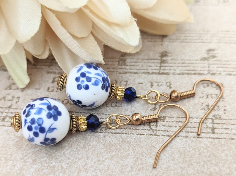 May include: A pair of gold dangle earrings with blue and white porcelain beads and blue crystal accents.