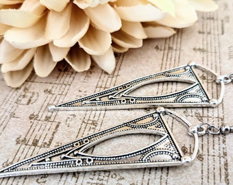 May include: A pair of silver triangle shaped earrings with intricate designs. The earrings have a hook closure.