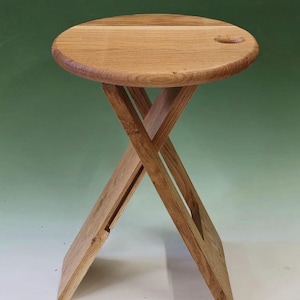 Könnte beinhalten: Kleiner, runder Beistelltisch aus Holz mit natürlicher Oberfläche. Die Tischplatte hat eine kleine, kreisförmige Vertiefung. Die Beine sind gekreuzt und bilden ein X. Der Tisch ist etwa 46 cm hoch.