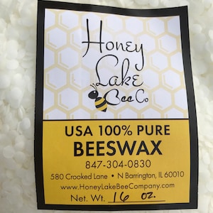 May include: A white label with black text and a honeycomb pattern reads "Honey Lake Bee Co. USA 100% Pure Beeswax 847-304-0830 580 Crooked Lane N Barrington, IL 60010 www.HoneyLakeBeeCompany.com Net. Wt. 16 oz."