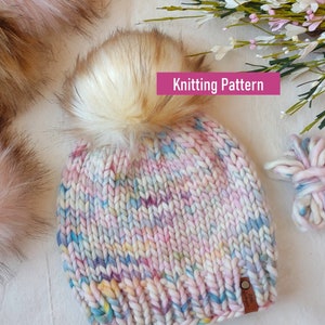 May include: A colorful knitted hat with a fluffy pom pom. The hat is made with a multi-colored yarn in shades of pink, blue, yellow, and white. The hat has a brown leather tag with the text "Little Alpaca" on it. Knitting Pattern.