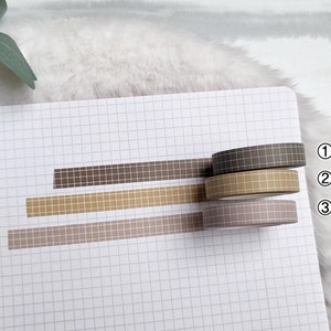 May include: Three rolls of patterned washi tape in brown, beige, and light brown. The tape has a grid pattern. The rolls are labelled 1, 2, and 3.
