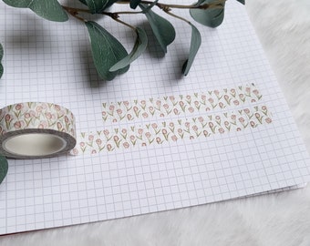 May include: A roll of washi tape with a floral pattern featuring pink flowers and green stems on a white background. The tape is on a gridded notebook.