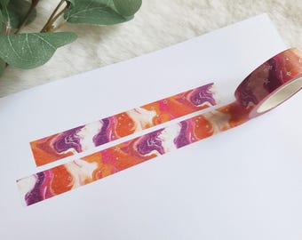 May include: A roll of washi tape with a colorful abstract design featuring swirls of orange, pink, and purple. The tape is partially unrolled, showing the pattern.