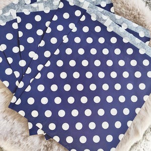 May include: Several navy blue paper gift bags with a white polka dot pattern are arranged on a fluffy, light-colored surface. The bags are open at the top, revealing a lighter-colored interior.