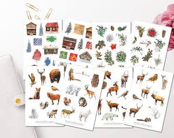 Könnte beinhalten: Mehrere Stickerbögen mit Aquarellillustrationen von Waldtieren, Hütten, Bäumen und Geschenken. Die Aufkleber sind auf weißen Hintergründen angeordnet, mit goldenen Büroklammern und einem weißen Planer im Hintergrund.