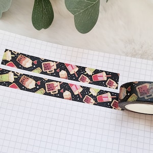 Könnte beinhalten: Eine Rolle schwarzes Washi-Tape mit einem sich wiederholenden Muster aus bunten Bubble-Tea-Bechern und Sternen. Das Band ist teilweise auf einer weißen, karierten Oberfläche abgewickelt.