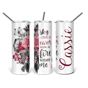 May include: A white stainless steel tumbler with a floral design and the text "Sky above me, earth below me, fire within me". The tumbler has a red lid and a straw. The tumbler is next to a white stainless steel tumbler with the text "Cassie" in red.