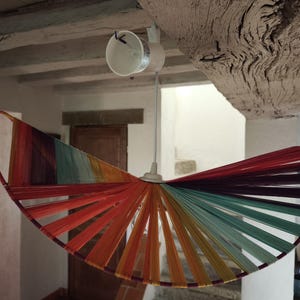 Peut inclure: Un luminaire suspendu fait à la main et coloré. Le luminaire présente un design semi-circulaire avec un spectre de couleurs, notamment le rouge, l'orange, le jaune, le vert et le violet. Il est suspendu au plafond par un cordon blanc et un luminaire blanc.