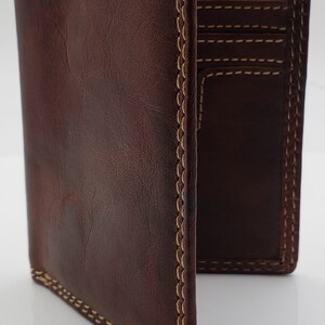 May include: A brown leather wallet with a stitched edge and multiple card slots. The wallet is folded open to show the interior.