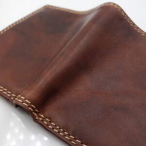 May include: A brown leather wallet with a light brown stitching detail around the edges.