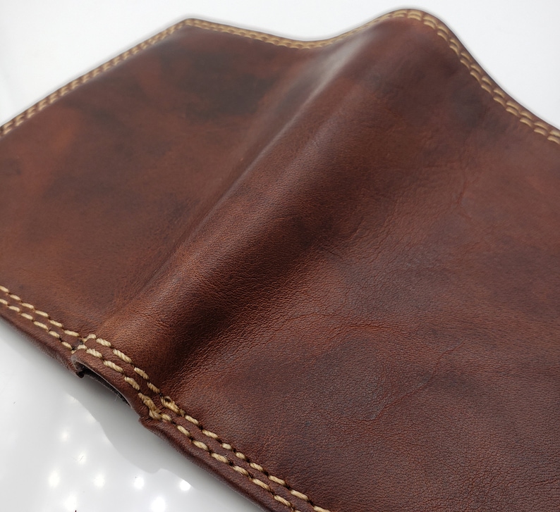 May include: A brown leather wallet with a light brown stitching detail around the edges.