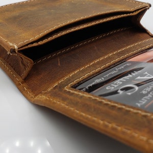 May include: A brown leather wallet with a stitched edge and a clear plastic window for an ID card. The window has the text "VALETS" and "DRIVER SAFETY" printed on it.