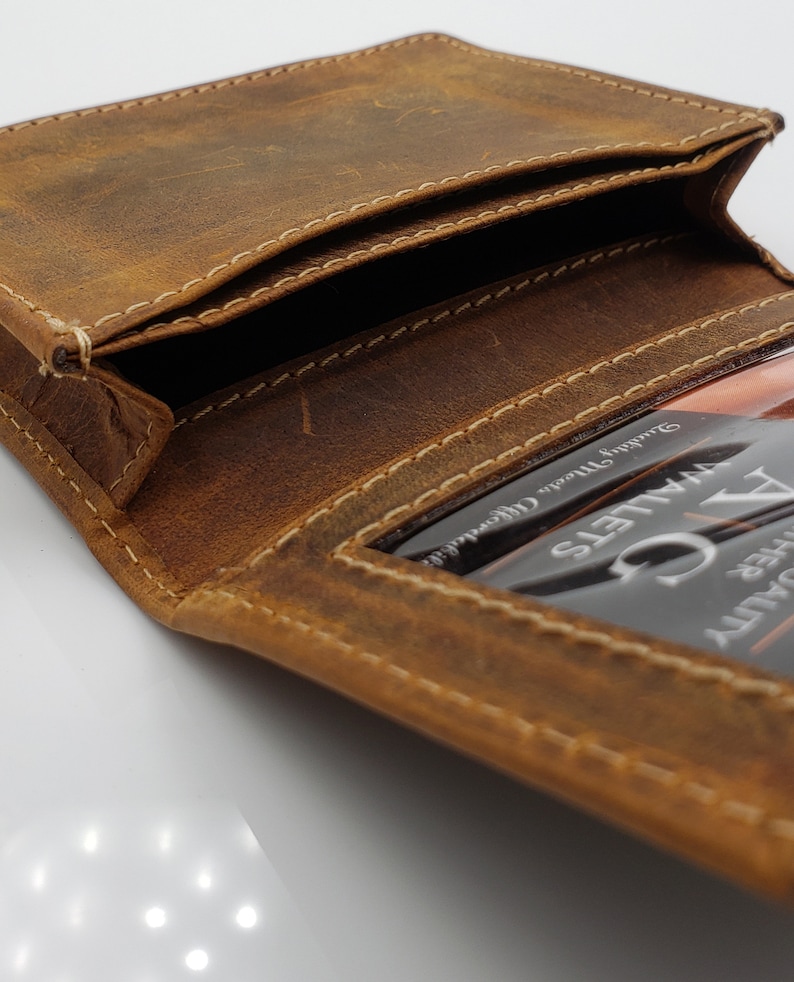 May include: A brown leather wallet with a stitched edge and a clear plastic window for an ID card. The window has the text "VALETS" and "DRIVER SAFETY" printed on it.
