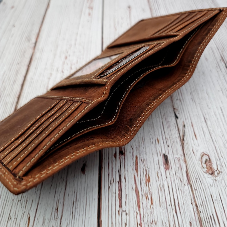 May include: Open brown leather wallet with multiple card slots and compartments. The wallet is made of distressed leather with white stitching. The interior features clear ID windows and additional storage. The wallet is displayed open, showcasing its interior design.