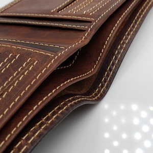 May include: A brown leather wallet with multiple card slots and a billfold. The wallet has a stitched edge with a contrasting light brown thread.